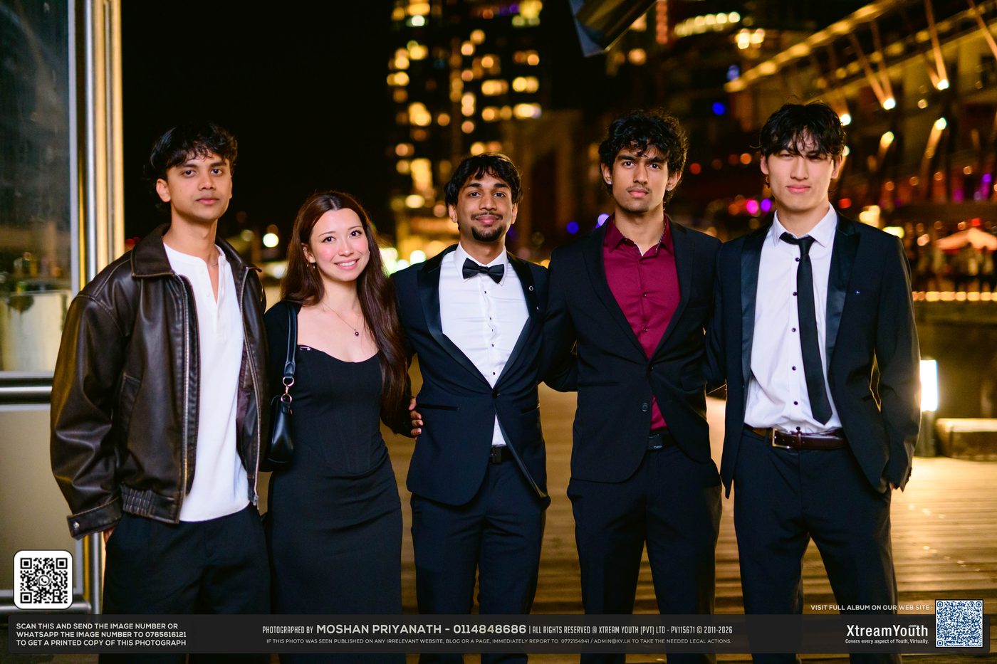 Five guests in black tie on the wharf, city lights behind them.