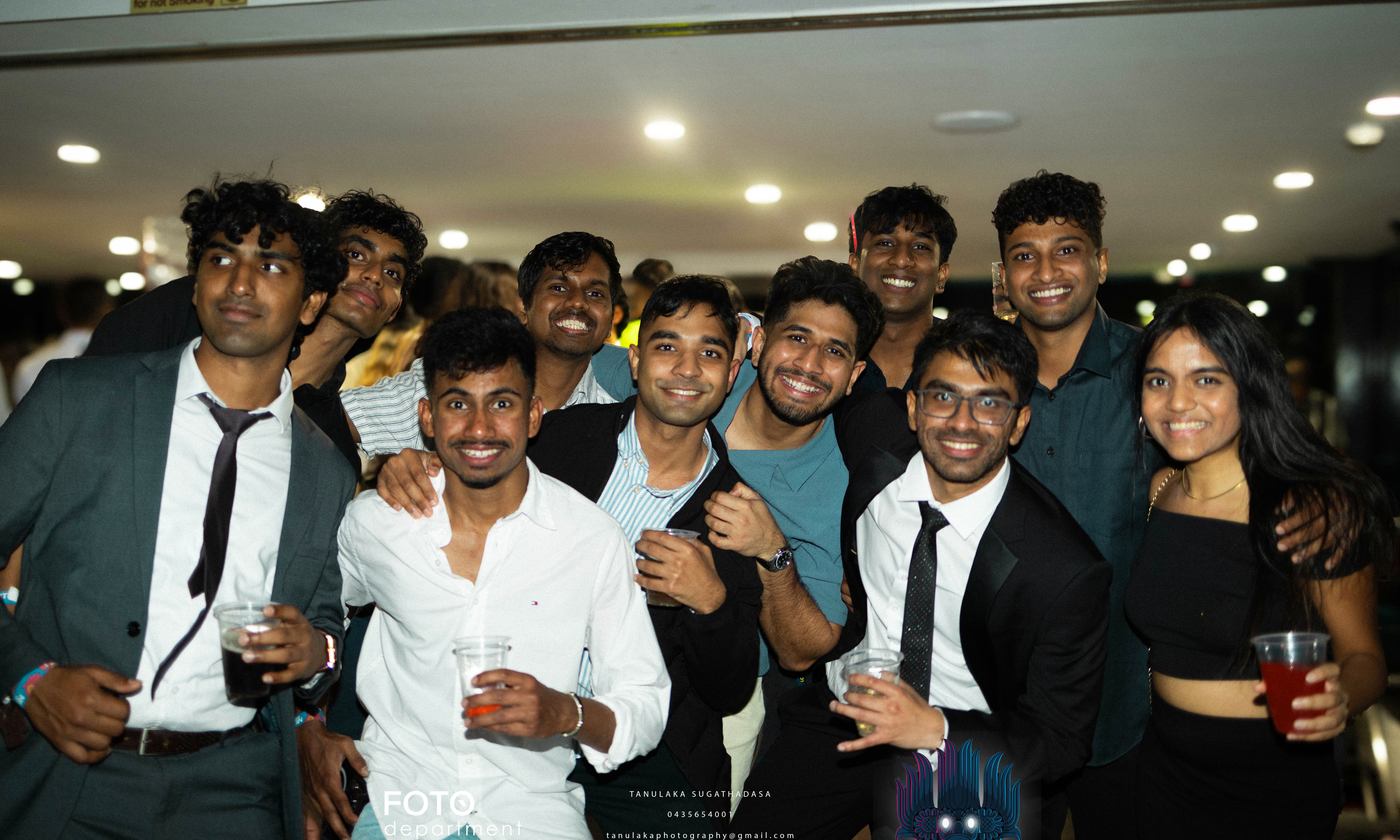 A large group packed together for a photo, drinks in hand, most in suits and formal dress.