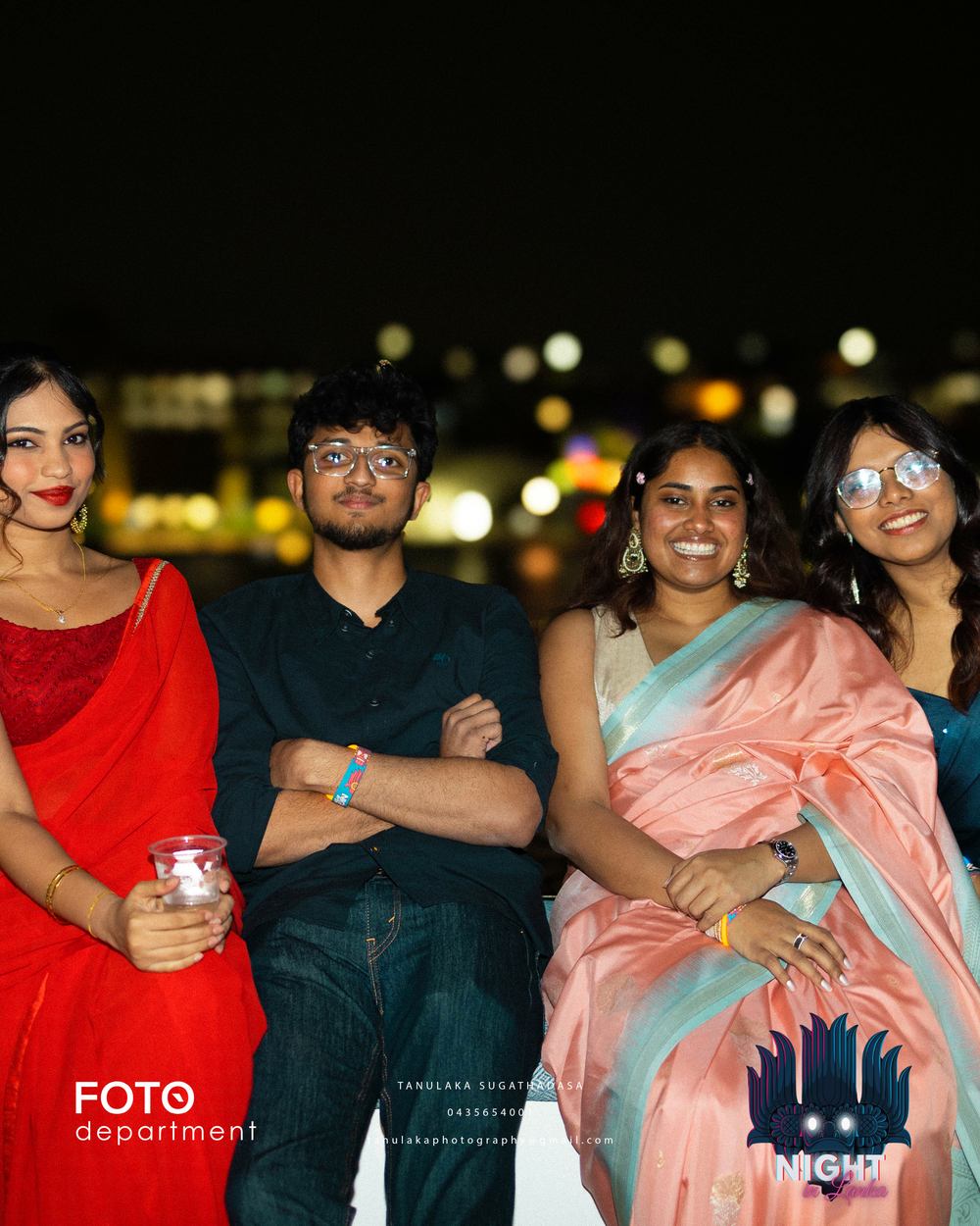 Friends on deck in saree and formal dress with the harbour lights behind them.